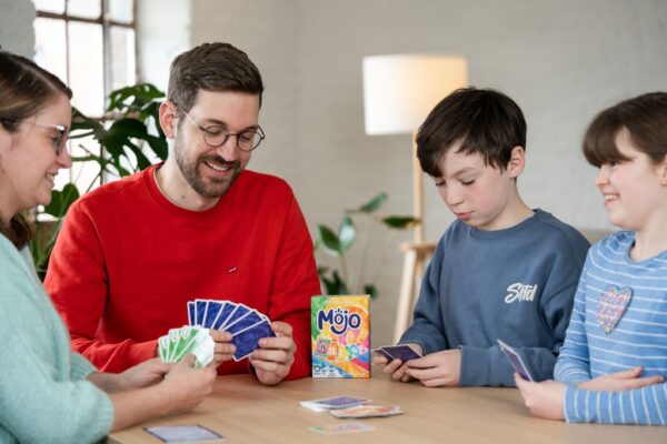 Photo d'une famille de 4, 2 adultes et 2 enfants, qui sont concentré en jouant sur une table au jeu de société Mojo