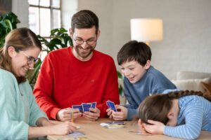 Photo d'une famille de 4, 2 adultes et 2 enfants, qui joue sur une table au jeu de société Mojo, la petite fille a perdu et a la tête dans ses bras